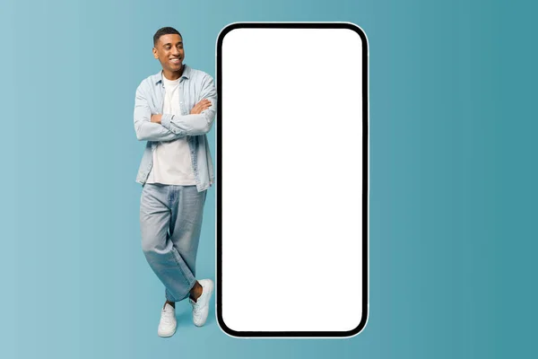 Cheerful confident African-American young man lean at huge smartphone with empty screen