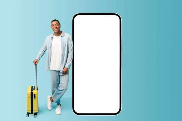 Smiling male African-American traveler with yellow suitcase lean at huge smartphone with empty screen — Stok fotoğraf