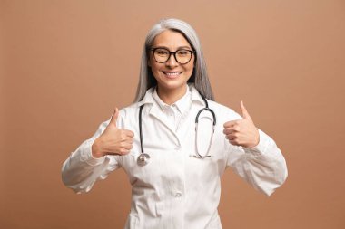 Neşeli orta yaşlı Asyalı kadın doktor baş parmağını kaldırıyor