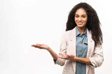 Afro saç stili olan, beyaz arka planda izole edilmiş, avuçlarında avuçlar olduğunu belirten çok kültürlü çekici bir kadın, gülümseyen kız öğrenci reklamcılığı.