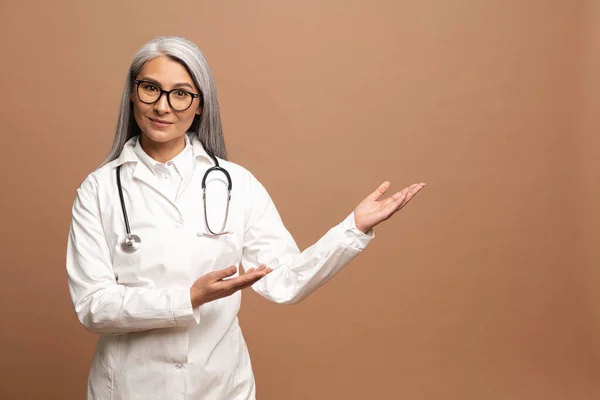 Asian charming female doctor pediatric, physician, therapist wearing a white medical gown with a stethoscope on the shoulders points hands on empty space — Stock Photo, Image