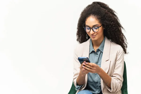 Веселая привлекательная брюнетка со смартфоном, наслаждающаяся чатом в социальных сетях, смс и улыбками, использующая мобильное приложение для знакомств по телефону, изолированная от белого — стоковое фото
