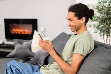 Genç ve yakışıklı Hintli serbest çalışan sosyal medyada sohbet etmek için akıllı telefon kullanıyor, mobil uygulama, alışveriş ya da mesajlaşma kullanıyor. Telefonu kullanan mutlu adam, haber yayını oturuyor