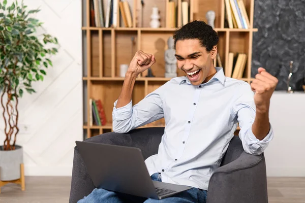We did it. Young man in casual shirt rejoicing at job success, a successful deal, and profit growth. He looking at the laptop screen and triumphantly — Foto Stock