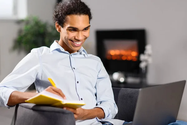 원거리에서 공부하고 일하기 위해 노트북 컴퓨터를 사용하는 젊고 곱슬머리 소년 이 행복하다. 웹 사이트를 보고 온라인 교육 과정을 수강하는 남자 — 스톡 사진
