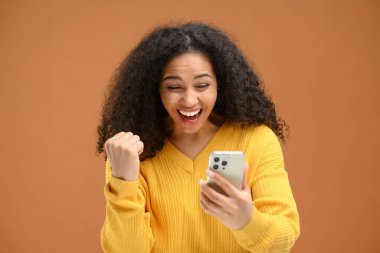 Şok olmuş genç bir kadın akıllı telefon ekranına bakıyor, ağzı açık bir şekilde seviniyor, kafası karışmış bir kadın telefona bakıyor.