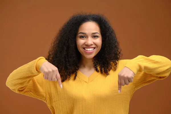 Çekici genç Afro-Amerikalı kadın işaret parmağı aşağı, kahverengi arka planda yenilik teşvik ediyor — Stok fotoğraf