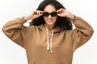 Beyaz tenli, kıvırcık saçlı, şık güneş gözlüğü takan Afro-Amerikalı genç bir kadın. 20 'li yaşlarda, çok kültürlü, gözlüklü bir kadın kameraya geniş bir gülümsemeyle bakıyor.