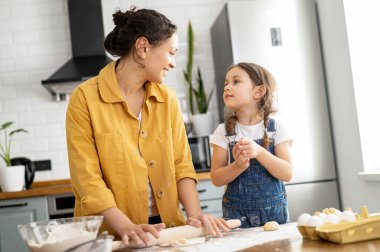 Anne ve küçük tatlı kızın şefkatli portresi, tatlı anne hamuru yoğurur, tapılası küçük kız ona yardım eder, birbirlerine bakar, evde boş vakitlerini kurabiye pişirerek geçirirler.