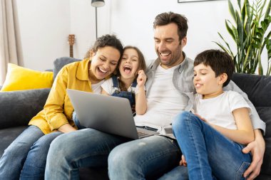 Dört kişilik mutlu bir aile rahat bir dairede dizüstü bilgisayar kullanıyor ebeveynler ve iki çocuk bilgisayar ve komedide film seyrediyor hafta sonlarını evde birlikte geçiriyorlar.