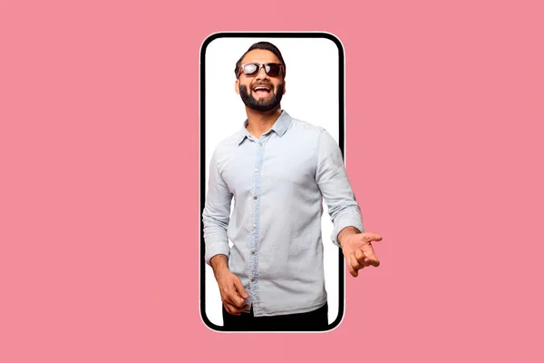 兴奋的印度小伙子戴着太阳镜 用想象中的吉他弹奏着用粉色隔开的巨大的手机 为新的移动应用 虚拟娱乐世界做广告 — 图库照片