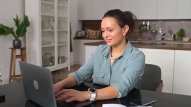 Smiling business woman using laptop for remote work from home. Confident lady checking emails, conducting business correspondence while sitting at the table, looking away
