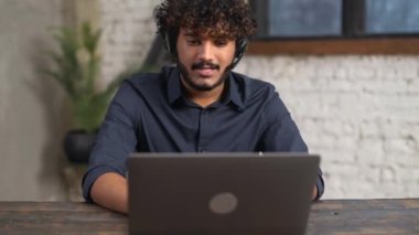 Ofisinde çalışan orta yaşlı Hintli bir adam, müşteri ve iş arkadaşlarıyla iletişim kurmak için kulaklık ve dizüstü bilgisayar kullanıyor. Gülümseyen çok ırklı doğulu adam bilgisayar ekranında telefonla konuşuyor.