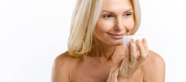 Hassas orta yaşlı bir kadın elinde nemlendirici zengin krem kavanozunu tutuyor, beyaza izole edilmiş, parfümünü soluyor, yeni kozmetoloji ürününü test ediyor ve reklamını yapıyor. Kişisel bakım kavramı