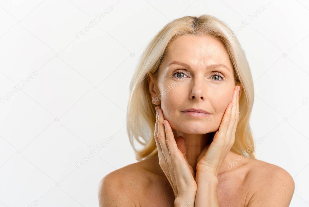 Attractive middle-aged blonde woman looking at the camera over white background, charming mature lady has calm and beautiful smile