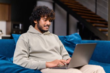 Uzaktan kumanda için dizüstü bilgisayar kullanan zeki bir Hintli serbest yazar. Yakışıklı sakallı adam internette sörf yapıyor, e-postaları gönderiyor ve cevaplıyor, kanepede otururken yazılım geliştiriyor.