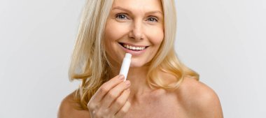 Mutlu ve iyimser orta yaşlı güzel kadın beyaza doğal dudak kremi sürüyor. Yakışıklı sarışın kadın nemlendirici ruj kullanıyor, tedavi kremi kullanıyor. Reklam kavramı