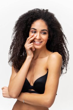 Çıplak omuzları olan, çok kültürlü, hoş görünümlü genç bir bayan neşeyle gülüyor. Beyaz arka planda izole edilmiş muhteşem afro-amerikan kadının resmi. Başka tarafa bakıyor ve dişlek gülümsüyor.