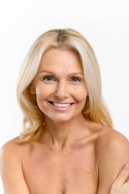 Çekici, orta yaşlı, çekici bir kadın beyaz arka planda kameraya bakıyor, çekici, olgun bir bayan nazikçe omzuna dokunuyor, güzel bir gülüşü ve sağlıklı dişleri var.