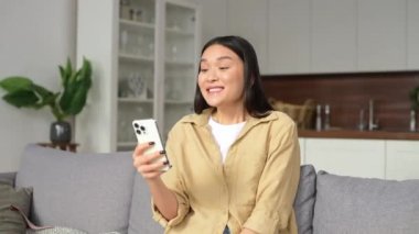 Genç ve güzel Asyalı bir kadın rahat koltukta oturmuş gülümsüyor ve elinde modaya uygun akıllı telefon tutuyordu. İnternetten arkadaşlarıyla konuşuyordu.
