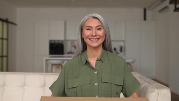 友善的白发女人鼓励与有需要的人分享东西 中年的亚洲女人看着坐在沙发上的相机 手里拿着印有题词的盒子 慈善概念 — 图库视频影像