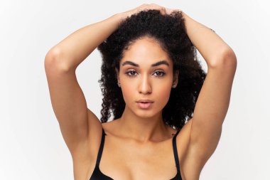 Çekici genç bayan kameraya bakıyor, saçının yakınında el ele tutuşuyor, izole bir şekilde. Stüdyoda beyaz arka planda poz veren güzel afro kadın.