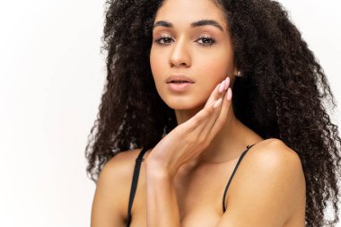 Beyaz arka planda izole edilmiş büyüleyici gülümseyen kadının belden yukarı portre görüntüsü. Kumral, kıvırcık saçlı, güzel bir bayan kameraya bakıyor ve yumuşak yüzünün yanında elini tutuyor.