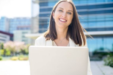 Açık havada dizüstü bilgisayar kullanan mutlu ve çekici bir bayan serbest yazar ya da öğrenci. Bilgisayarlı neşeli kadın kameraya bakıyor ve gülümsüyor.