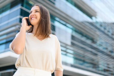 Sokakta yürürken akıllı telefondan konuşan mutlu, çekici bayan serbest çalışan ya da öğrenci, iş kadınının dışarıda hoş bir telefon konuşması var. Neşeli bir kadın telefonda konuşuyor.