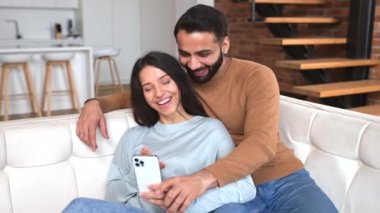 Olumlu Hintli çift evde birlikte vakit geçirir, akıllı telefonu web sörfü için kullanır, Pakistanlı erkek ve kadın birlikte telefon ekranına bakar, haberleri kaydırır, ya da internetten smth 'i seçer.
