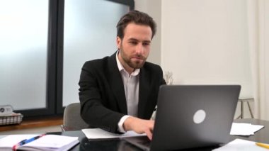 Crazy excited lucky young bearded businessman sitting at the desk with laptop, raised fists up celebrating success, making yes gesture, got job promotion, got promoted, won lottery, victory concept