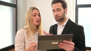 Güzel bir kadın ve elinde dijital tabletle ciddi bir adam ofiste dikilip tablet ekranı izliyor ve kafası karışık hissediyor.