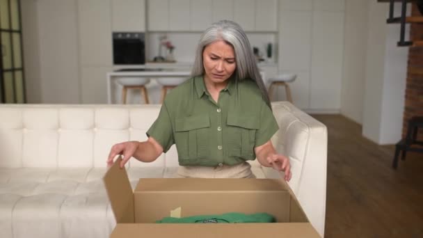 一位失望的亚洲中年女士对网上购物感到不安 头发灰白的女人看着纸板箱里面 对错误的定单感到不快和愤怒 — 图库视频影像