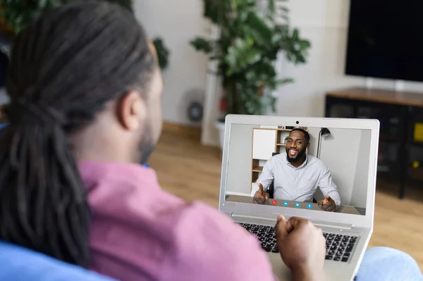 Two male African-American male friends using computer app for video meeting, talking online, has virtual discussing. Black man holding video call on the laptop, back view
