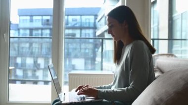 Odaklanmış serbest çalışan kadın uzaktan çalışıyor, evdeki kanepede oturan dizüstü bilgisayarda daktilo kullanıyor, internetten mesajlaşan, e-posta gönderen ya da konu hazırlayan konsantre kız öğrencilere yandan bakıyor.