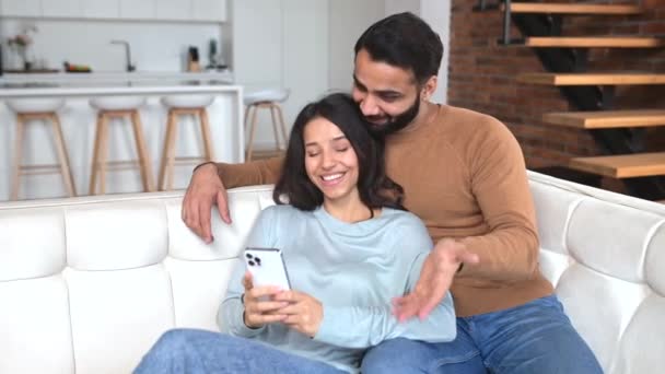 Young Cheerful Indian Couple Sitting Sofa Cozy Living Room Using — Vídeo de Stock