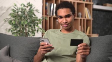 Çevrimiçi ödeme için akıllı telefonu kullanan genç, yakışıklı serbest çalışan, kredi kartı tutuyor ve veri girişi yapıyor, yiyecek, alışveriş ve satın alma için uygulama kullanıyor