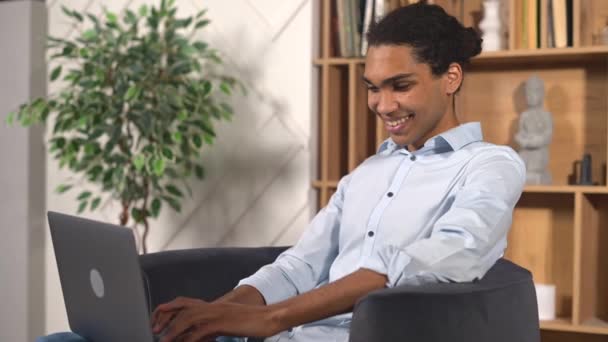若い多人種男性の学生は ウェブセミナー 教育コースを見て 距離について学び 電子メールを入力します ソファに座っている間 ラップトップを使用してカジュアルウェアで楽観的な民族の男 — ストック動画