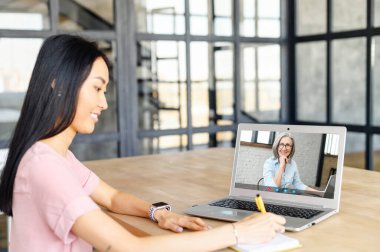 Genç Asyalı bir kadın İngilizce öğretmeni ve öğretmeniyle uzaktan iletişim kurmak için başvuruda bulunuyor. İnternetten patronla konuşuyor, sanal bir ders alıyor, evden ders çalışıyor ve notlar alıyor.