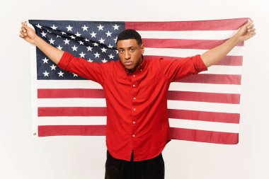 Serious African-American guy holding in hands american flag isolated over white background, multiracial foreign student man holding US flag, independence day celebration, holiday