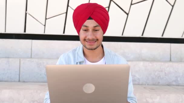 Cheerful Indian Man Wearing Headwrap Sitting Steps Outdoors Using Laptop — Stockvideo