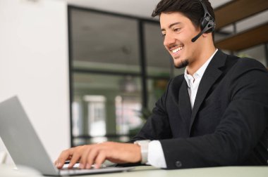 İş arkadaşları ya da müşterileriyle iletişim kurmak için laptop kullanan kulaklıklı arkadaş canlısı Latin erkek ofis çalışanı, video konferansında yer alıyor. Bir destek subayı bir müşteriyle konuşuyor, yardım hattı.