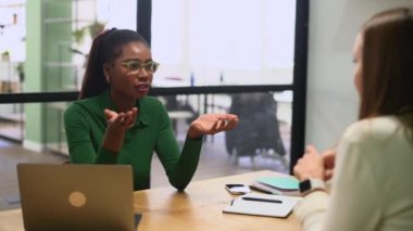 High-skilled female employee explaining something to coworkers during morning meeting, confident african-american businesswoman talking and gesturing, presenting her ideas
