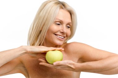 Güzel, olgun, 50 'li yaşlarda, iki eli de taze yeşil elma tutan bir kadın. Beyaz üzerinde çıplak omuzları olan orta yaşlı bir model pürüzsüz ve ışıl ışıl bir cilde sahip. Antiyaj tedavisi
