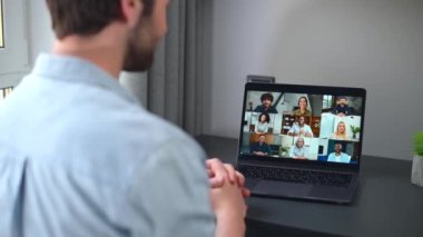 Virtual conference, online meeting. Young man using computer app for communicating with many people at same time together. Back view. Video call with diverse employees