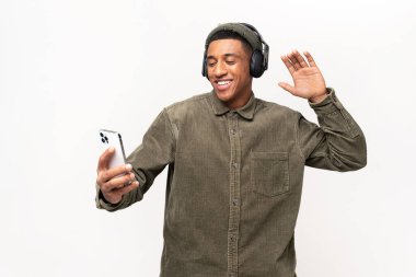 Sevinçli, neşeli, çok kültürlü, favori şarkıları dinleyen, beyaz üzerinde tek başına dans eden adam. Kablosuz kulaklık takan neşeli Latin adam akıllı telefonu elinde tutuyor ve müziğin tadını çıkarıyor.