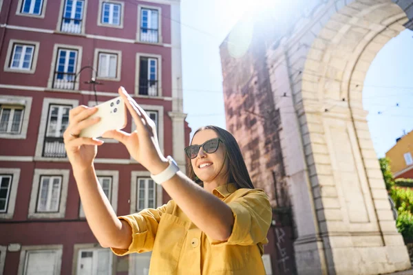 Overjoyed happy foreign woman tourist taking photo with trendy smartphone, walking in old town of Lisbon, Portugal