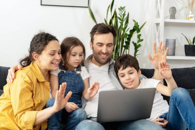 Sanal toplantı. Büyükanne ve büyükbabasıyla video bağlantısı için dizüstü bilgisayar kullanırken dört kişilik bir aile ekranda el sallıyor. Çok ırklı anne, baba ve iki çocuk dizüstü bilgisayarlarında el sallıyorlar.