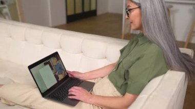 Son sınıf öğrencisi bir kadın kanepeye uzanıp, erkek öğretmenle eğitim dersleri almak için dizüstü bilgisayar kullanıyor. Orta yaşlı kız öğrenci