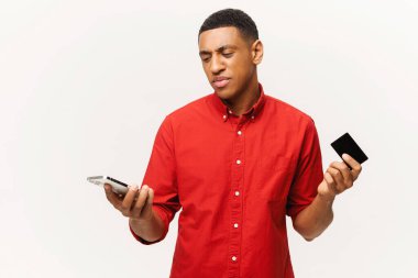 Latin adam para için endişeleniyor. Kredi kartı ve akıllı telefonu olan kafası karışmış bir adam hayal kırıklığına uğramış bir yüz, omuz silkme, iflas konsepti.